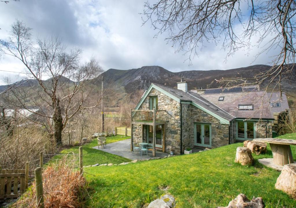 a stone house on a hill with mountains in the background at Tyn y Maes in Bethesda