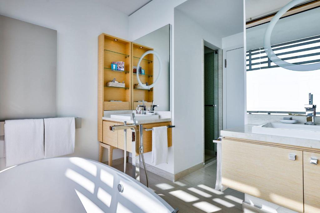 a bathroom with a sink, tub, and a window at BUDERSAND Hotel - Golf & Spa - Sylt in Hörnum