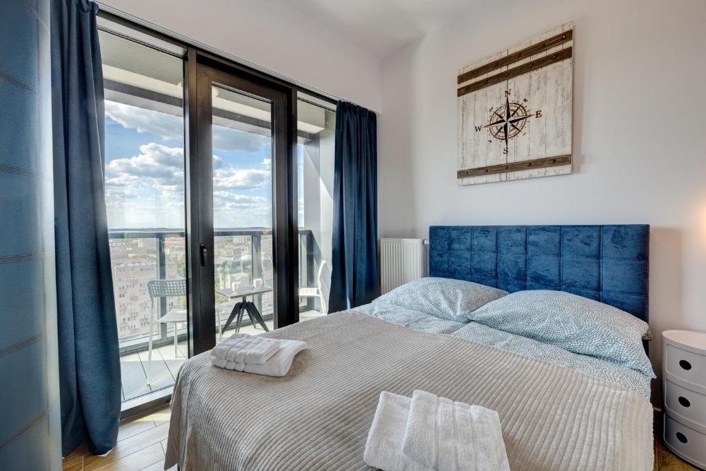 a bedroom with a blue bed and a large window at Aleda Hanza 14 floor, balkon in Szczecin