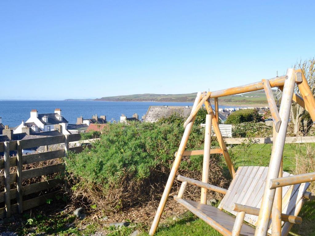 a wooden bench sitting on a hill next to the ocean at Pebble Cottage in Port William