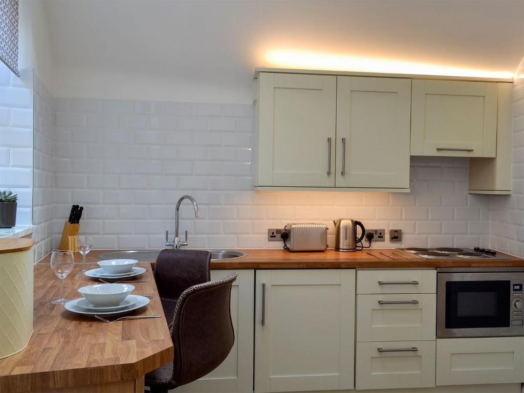 a kitchen with white cabinets and a wooden table at Kinder Apartment - Uk12957 in Glossop