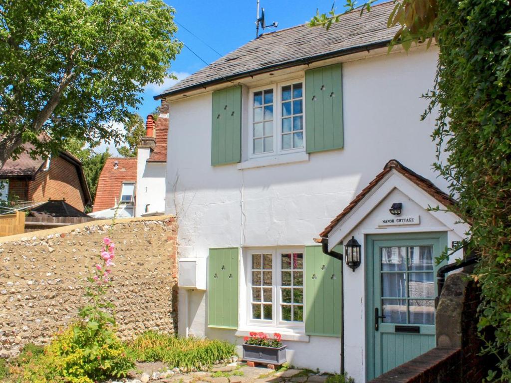 a cottage with green shutters and a stone wall at Manor Cottage in Findon