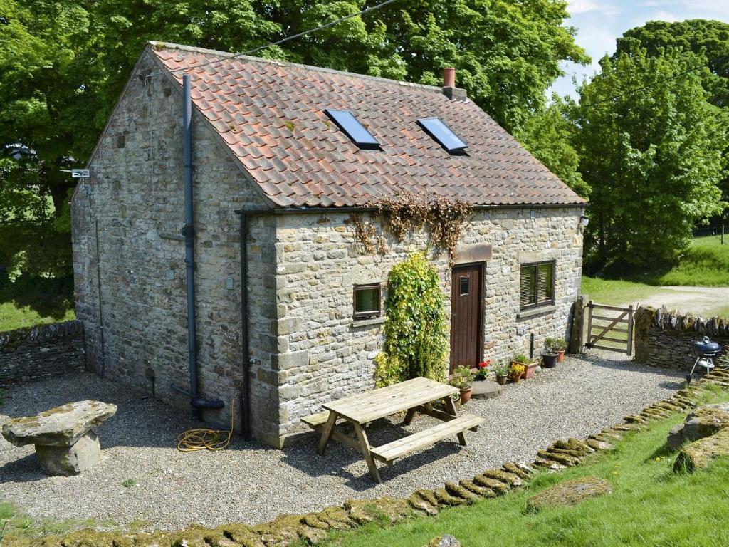 un pequeño edificio de piedra con un banco y una mesa en Grange Farm Cottage, en Barton in the Clay