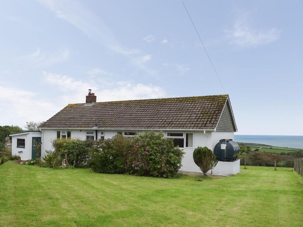 una casa blanca con un patio verde y el océano en Arforwest en Llangranog