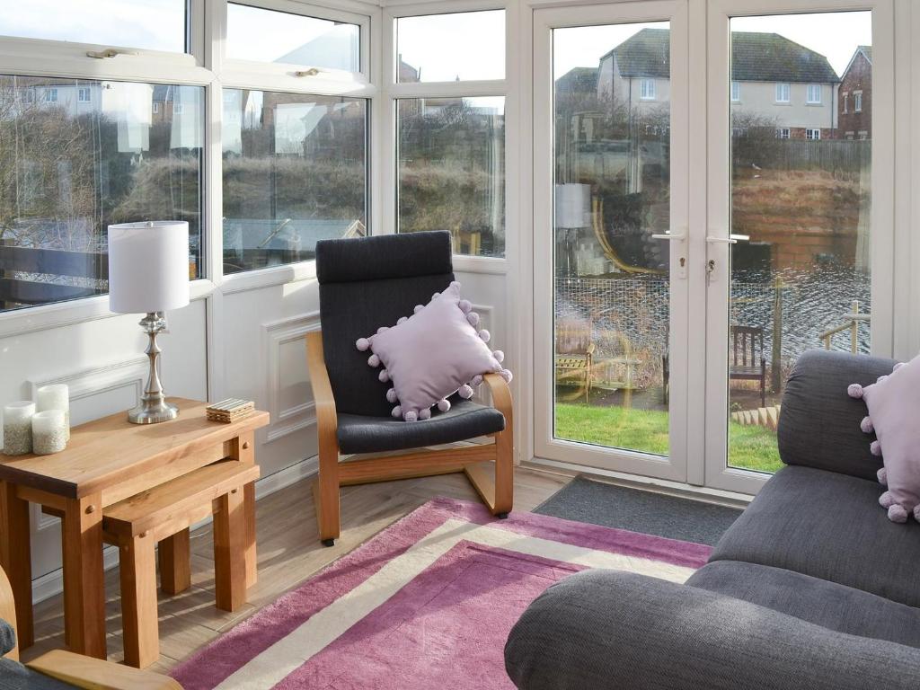 a living room with a chair and a table and windows at Spring Tides in Beadnell