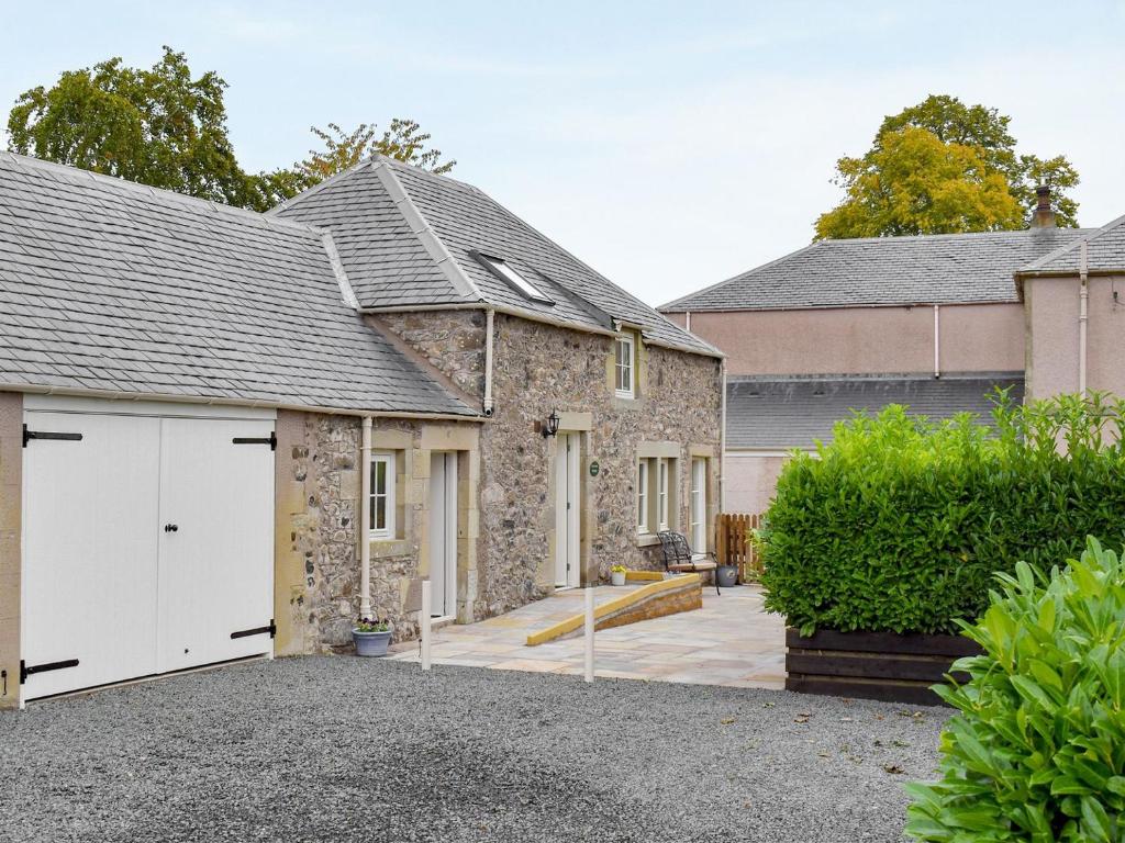 a stone house with white garage doors in a driveway at Grooms Bothy in Nenthorn