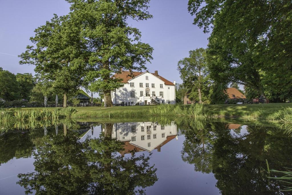 una casa reflejada en el agua de un lago en Hotel & Gästehaus Gut Kaden, en Alveslohe