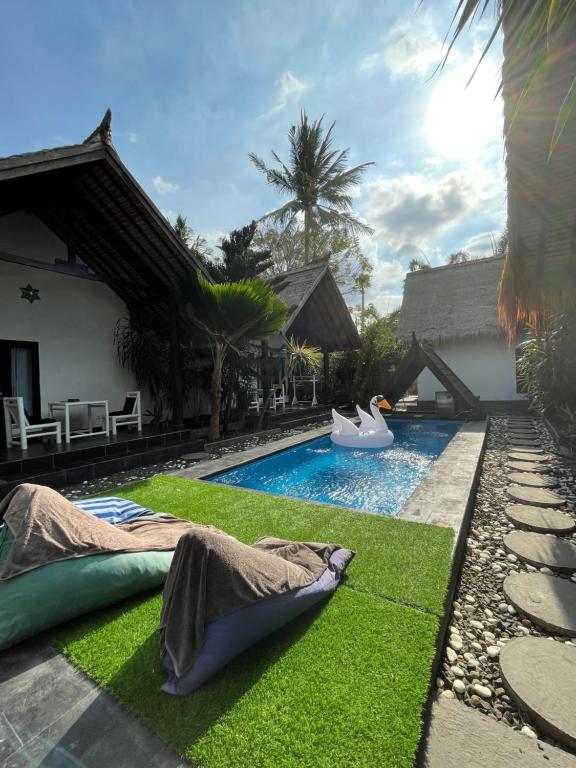 a backyard with a pool with green grass and a swimming pool at Black & White Cottages in Gili Trawangan