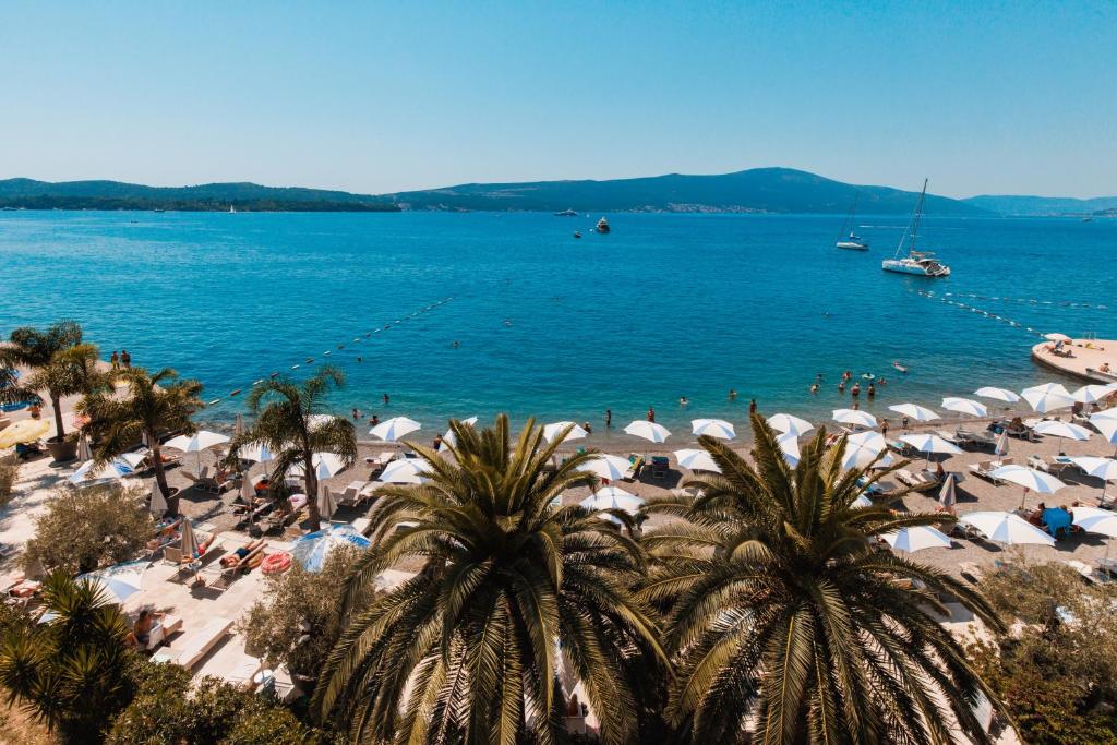 a beach with umbrellas and people on the water at Hotel Palma in Tivat