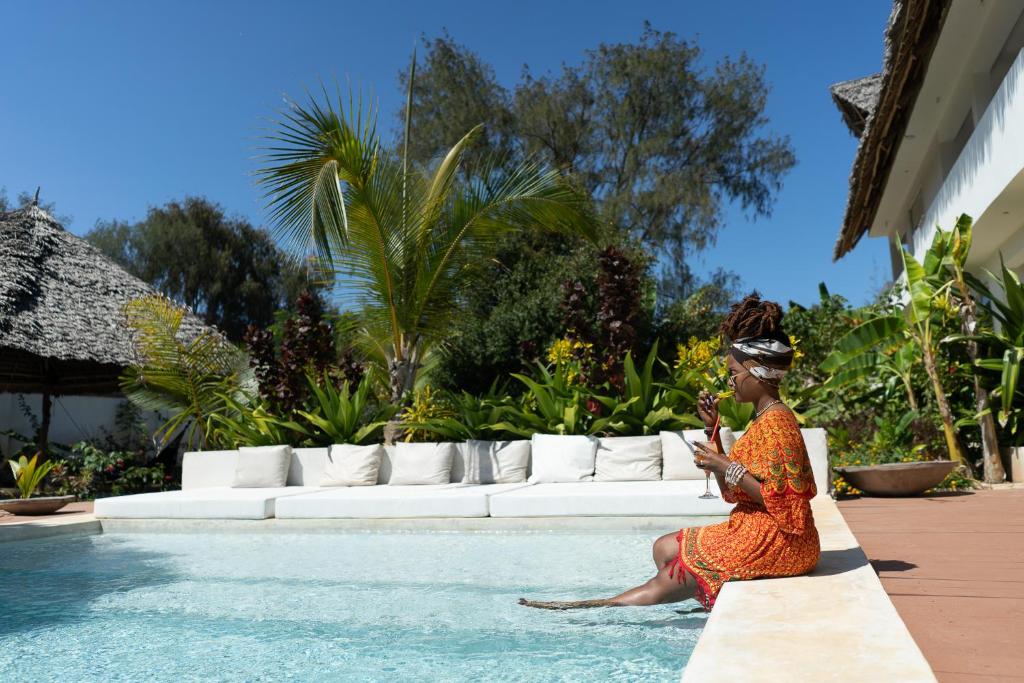 una mujer sentada en una cornisa junto a una piscina en Kuwa Zanzibar en Kiwengwa