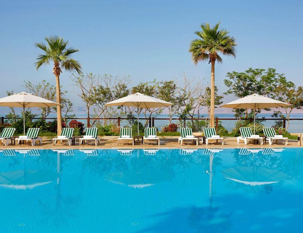 a swimming pool with chairs and umbrellas and palm trees at Holiday Inn Resort Dead Sea, an IHG Hotel in Sowayma