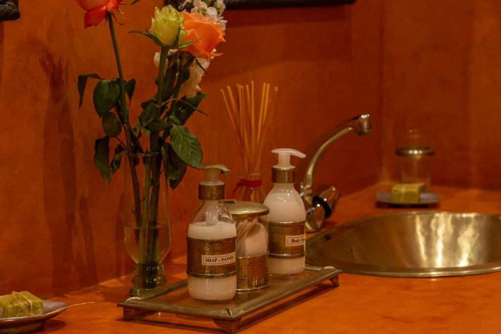 een wastafel met drie flessen zeep en een vaas met bloemen bij Riad Dar Talah in Marrakesh