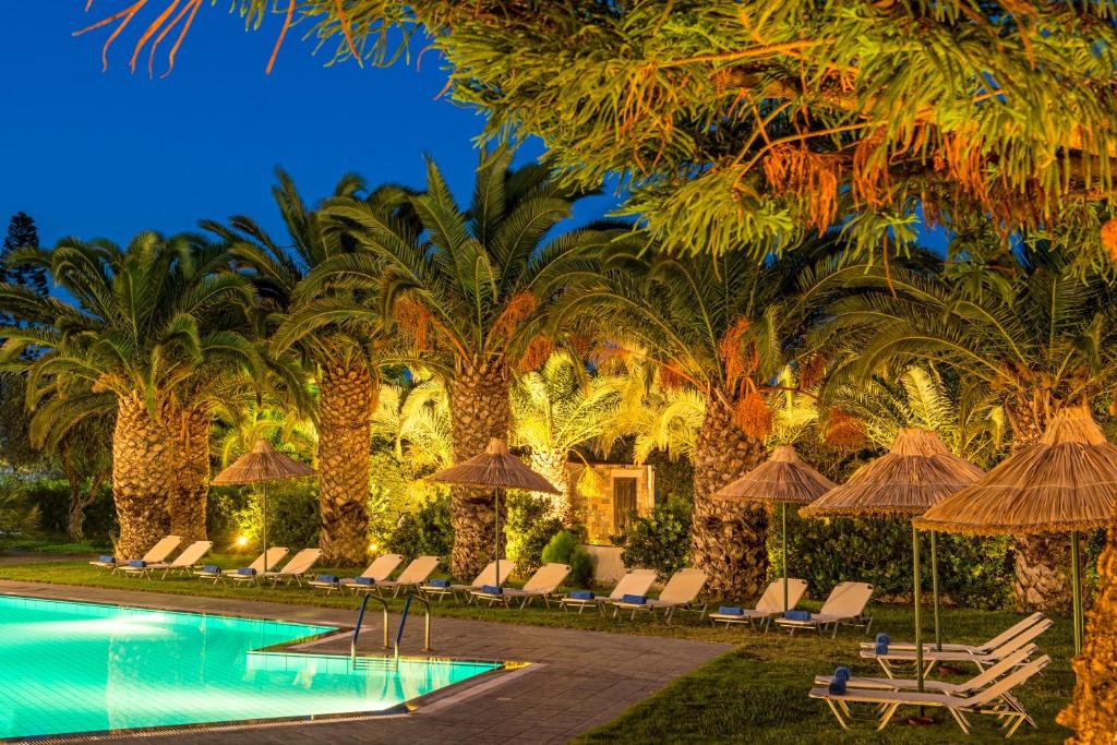 a pool with chairs and umbrellas and palm trees at Hersonissos Maris in Hersonissos
