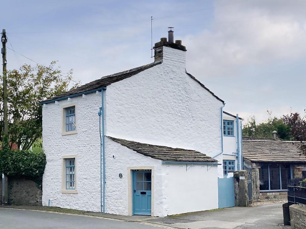 a white house with a blue door on a street at The White Cottage in Gargrave