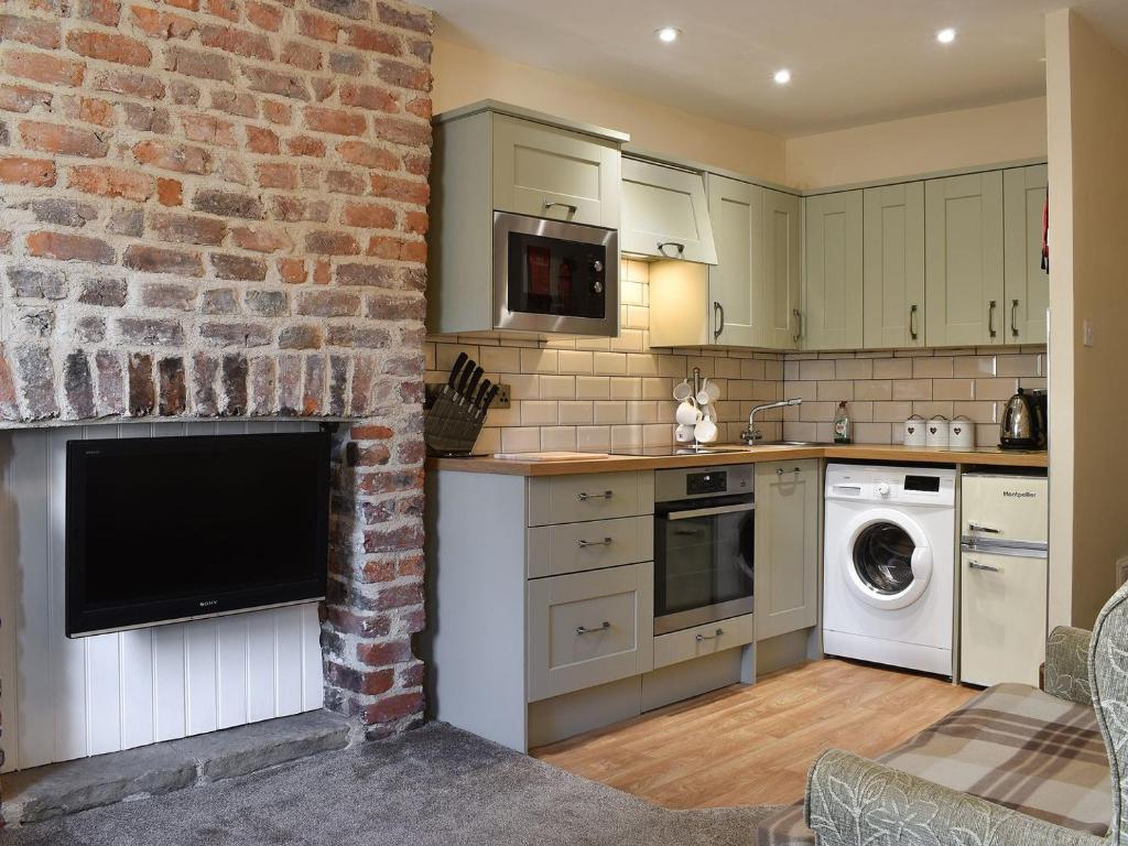 a kitchen with a brick wall with a tv on a fireplace at Caedmons Dream in Whitby