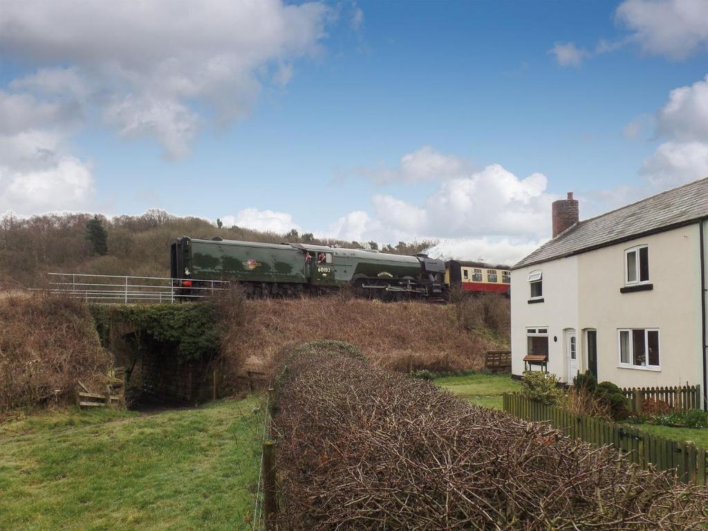 a train traveling past a white house and a building at Cobbs Cottage in Grosmont