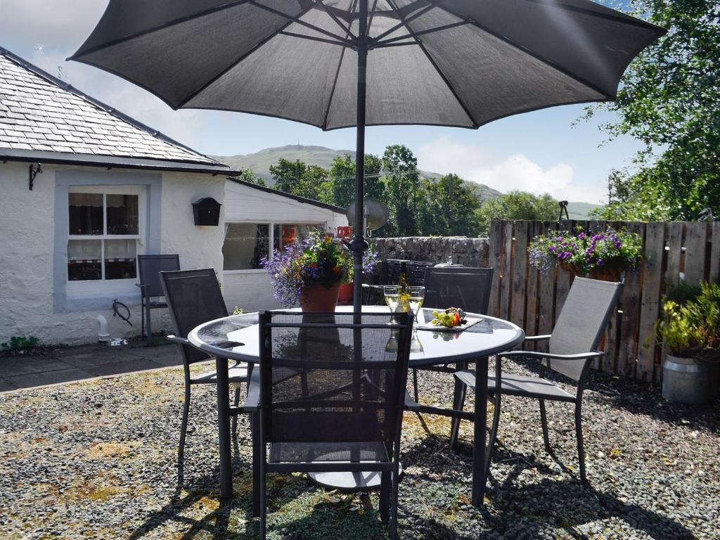Belstane Cottage في Straiton: طاولة وكراسي مع مظلة في الفناء