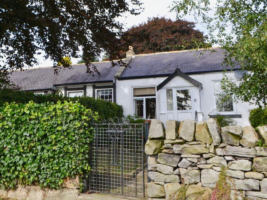 a white house with a stone wall and a fence at Fairground Cottage in Rothbury