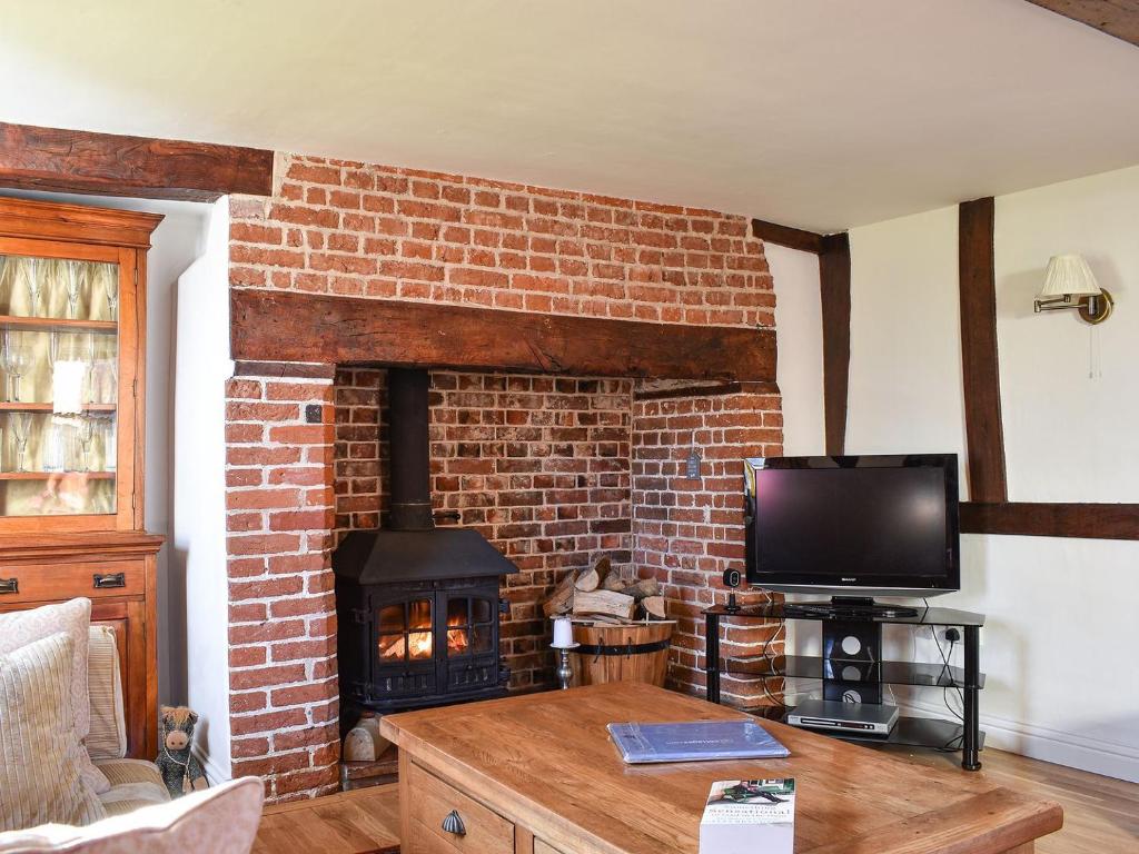 a living room with a brick fireplace and a tv at Brushmaker Cottage in Diss