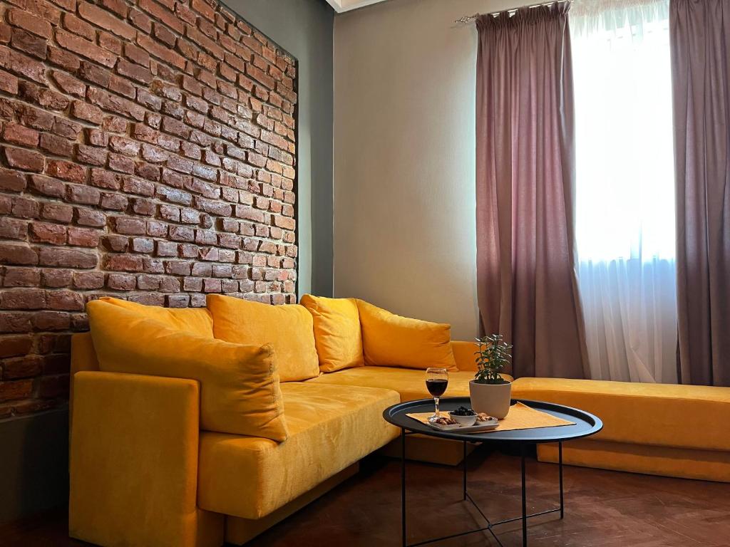 a living room with a yellow couch and a brick wall at Gramophone Apartments in Bitola