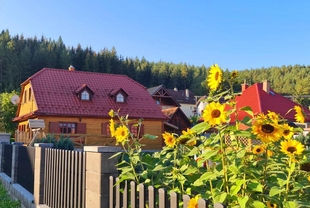 a wooden house with a fence and sunflowers at Holidayhouse Chalupa Alžbetka in Važec