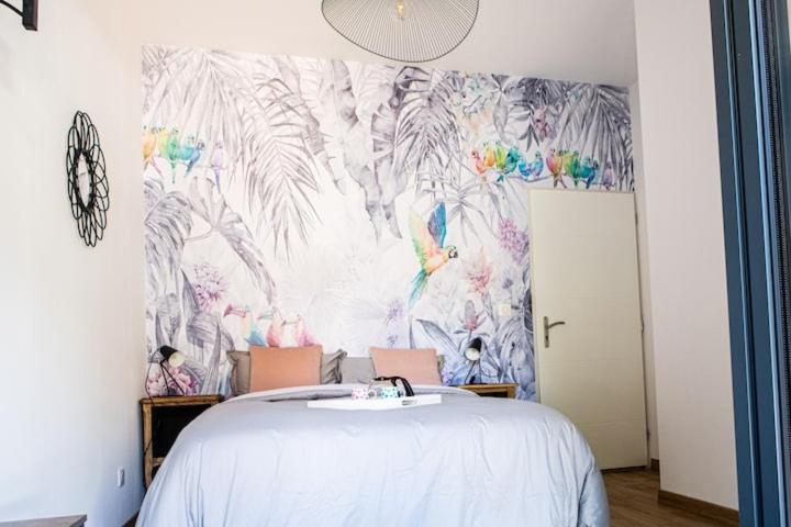 VinzellesにあるChambre tropicale privée au coeur d'un village calme et proche du vignobleのトロピカルな壁紙の白いベッドが備わるベッドルーム1室が備わります。