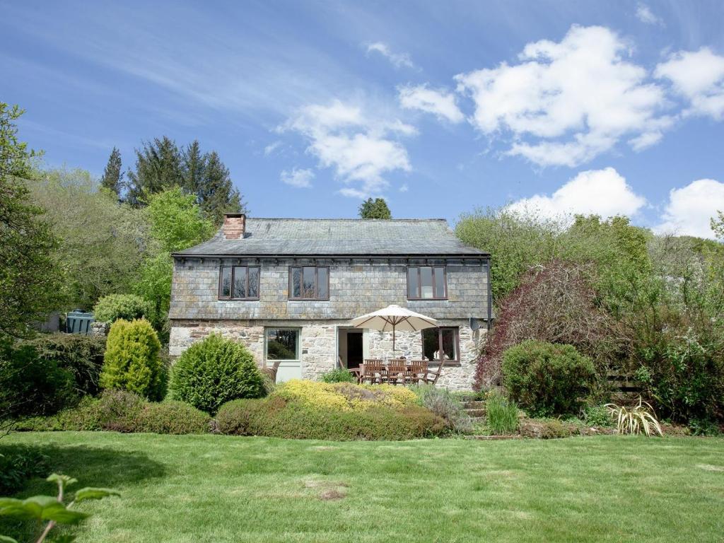 an old stone house with an umbrella in a yard at Coach House - Uk32684 in Sheepstor