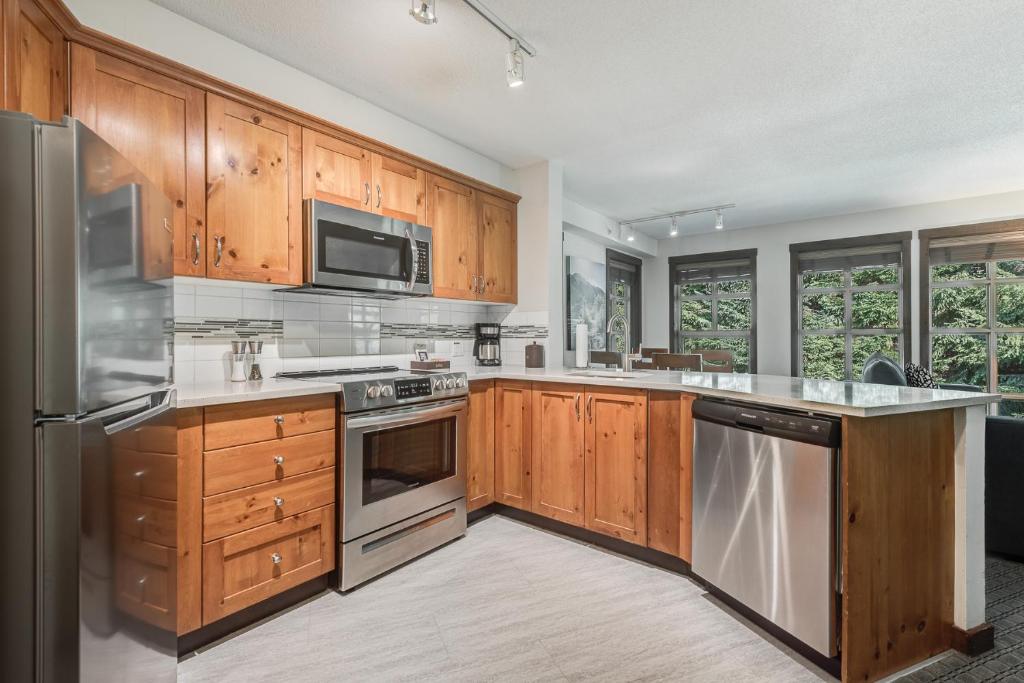 a kitchen with wooden cabinets and stainless steel appliances at Blackcomb Springs Suites by CLIQUE in Whistler