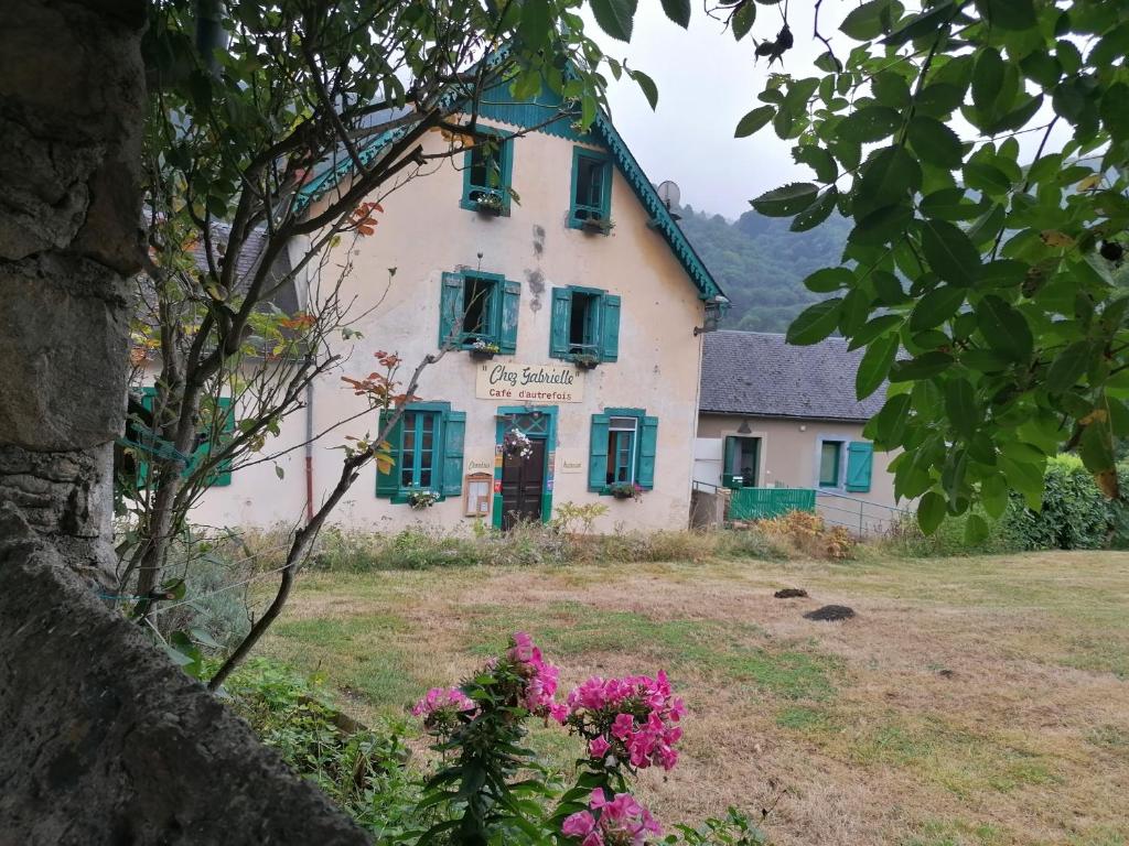 una casa antigua con flores y ventanas con contraventanas verdes en Auberge Chez Gabrielle - Vallée de Lesponne, en Beaudéan