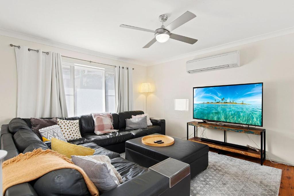 a living room with a black couch and a flat screen tv at Summerside 43 Lentara Street in Fingal Bay