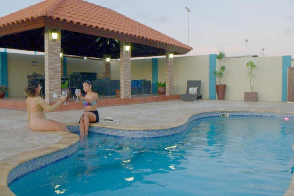 two women sitting on the edge of a swimming pool at Enjoyment Villa Cataleya in Oranjestad