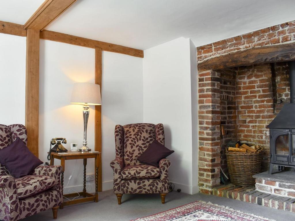 a living room with two chairs and a brick fireplace at Holme Cottage in Eastry