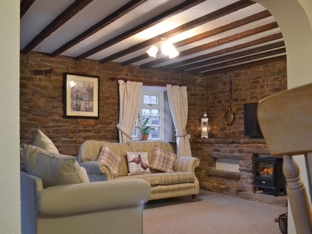 a living room with a couch and a brick wall at Ivy Cottage in South Wingfield