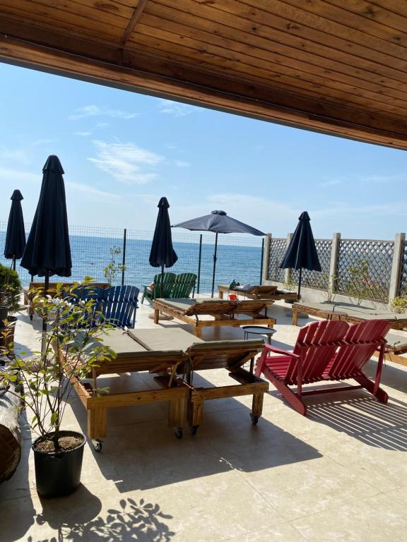 eine Terrasse mit Tischen, Stühlen und Sonnenschirmen und dem Meer in der Unterkunft Claude Monet Seaside Hotel in Grigoleti