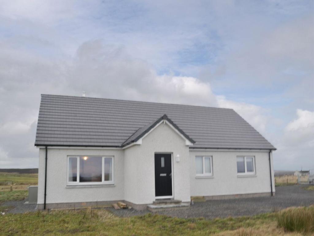 a white house with a black roof in a field at Claymore Cottage in Whaligoe