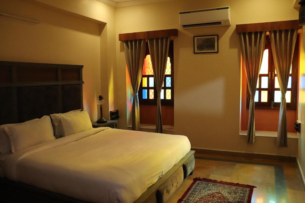 a bedroom with a large bed and two windows at BALARWA HAVELI in Jodhpur