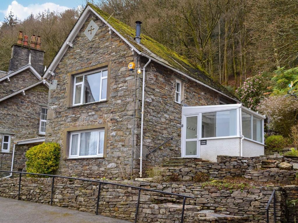 a stone house with white windows and a stone wall at The Coach House - Uk30813 in Braithwaite