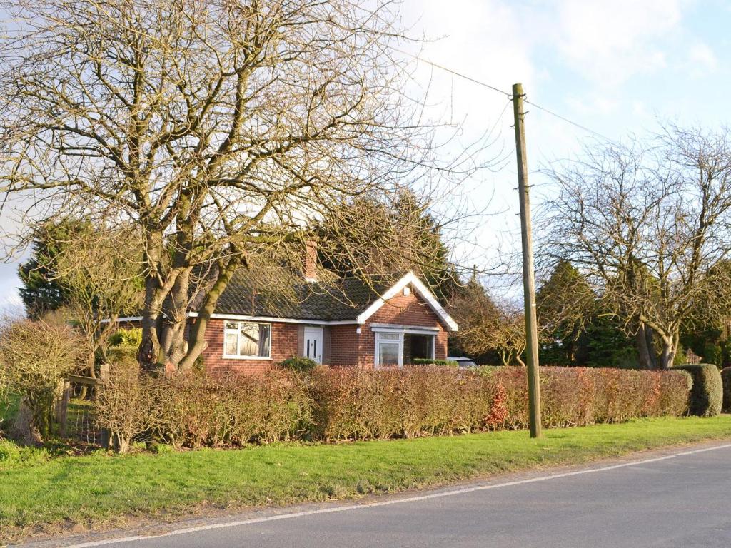 a house on the side of a road with a hedge at Wayside Cottage in Beeford