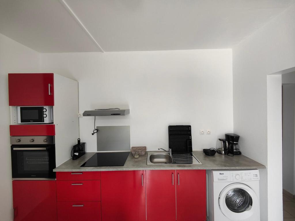 a kitchen with red cabinets and a washing machine at Rayon de soleil 1 chambre bas de villa in Sainte-Anne
