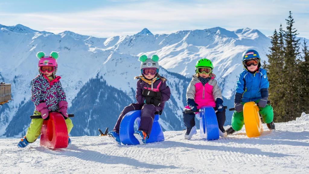 a group of four children sitting in the snow on snowboards at Hotel Steinbock in Klosters