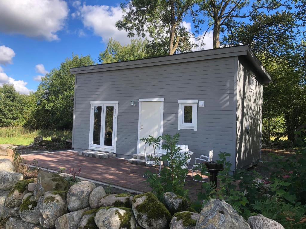 uma pequena casa cinzenta com um deque de madeira em Kattalängan - Lilla huset em Brösarp