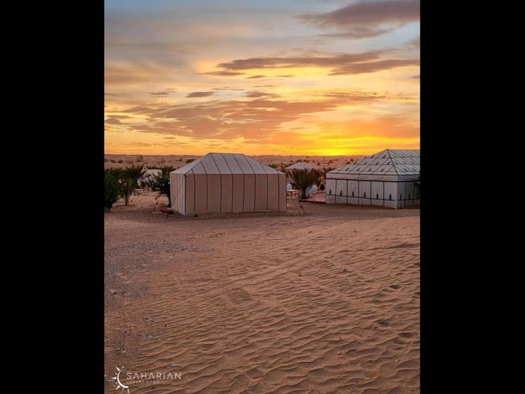 two buildings on a beach with a sunset in the background at Splendid desert Saharian Luxury Camp in quiet and idyllic sand dunes in Tisserdmine