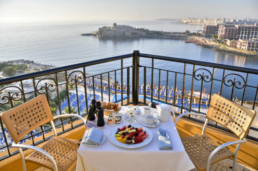 a table with a plate of food on a balcony at Corinthia St George's Bay in St. Julianʼs