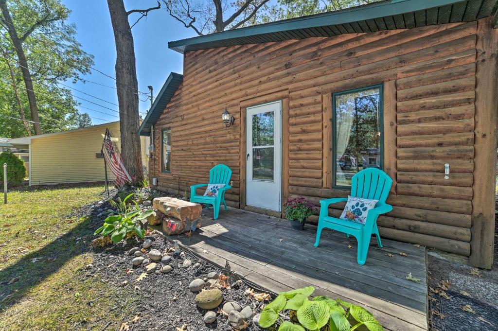 una cabina di legno con due sedie blu sulla veranda anteriore di Charming Houghton Lake Cottage with Backyard! a Houghton Lake
