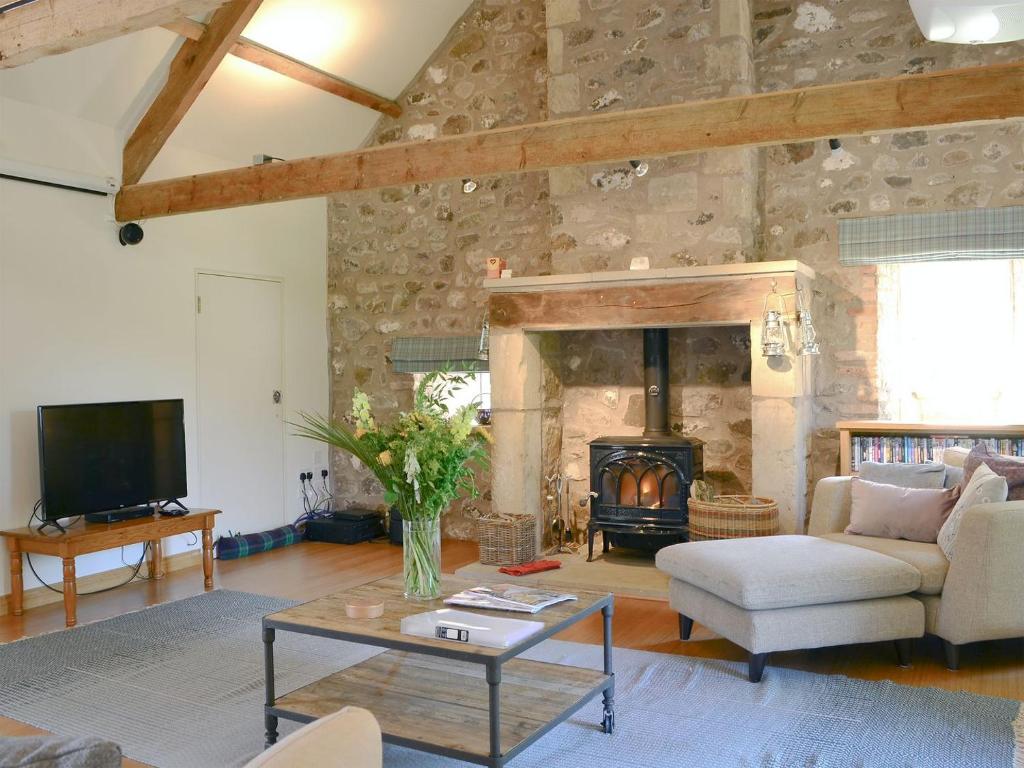 a living room with a stone wall with a fireplace at Longknowe Barn in Branxton