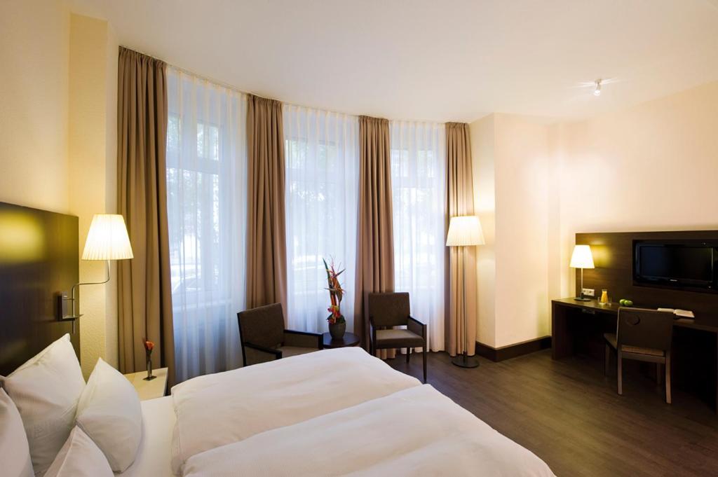 a hotel room with a large white bed and a desk at Villa Hotel Frankfurt by MZ HotelCollection in Frankfurt