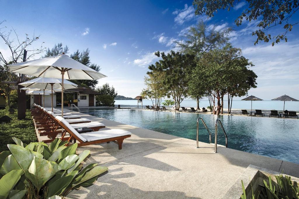 a pool with benches and umbrellas next to the water at Centara Chaan Talay Resort And Villas Trat in Ban Khlong Muang