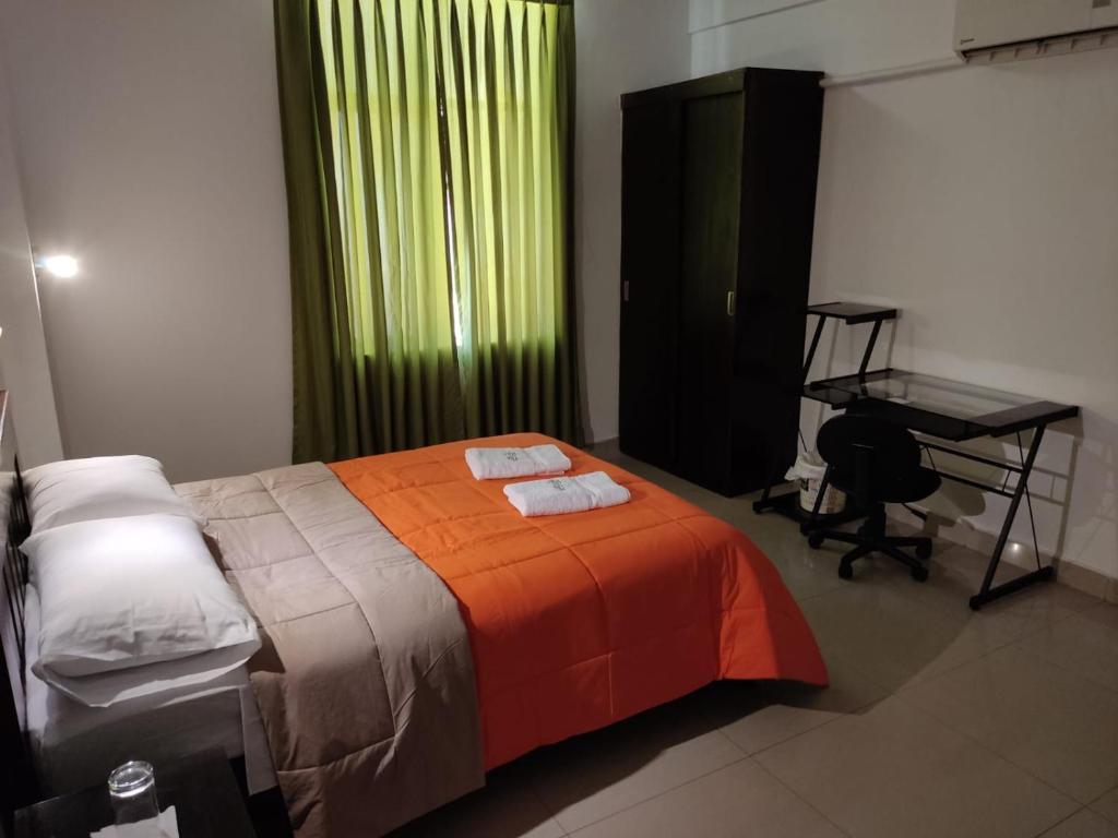 1 dormitorio con 1 cama con manta naranja y escritorio en HOTEL PUNTA PARIÑAS-TALARA-PERU, en Talara