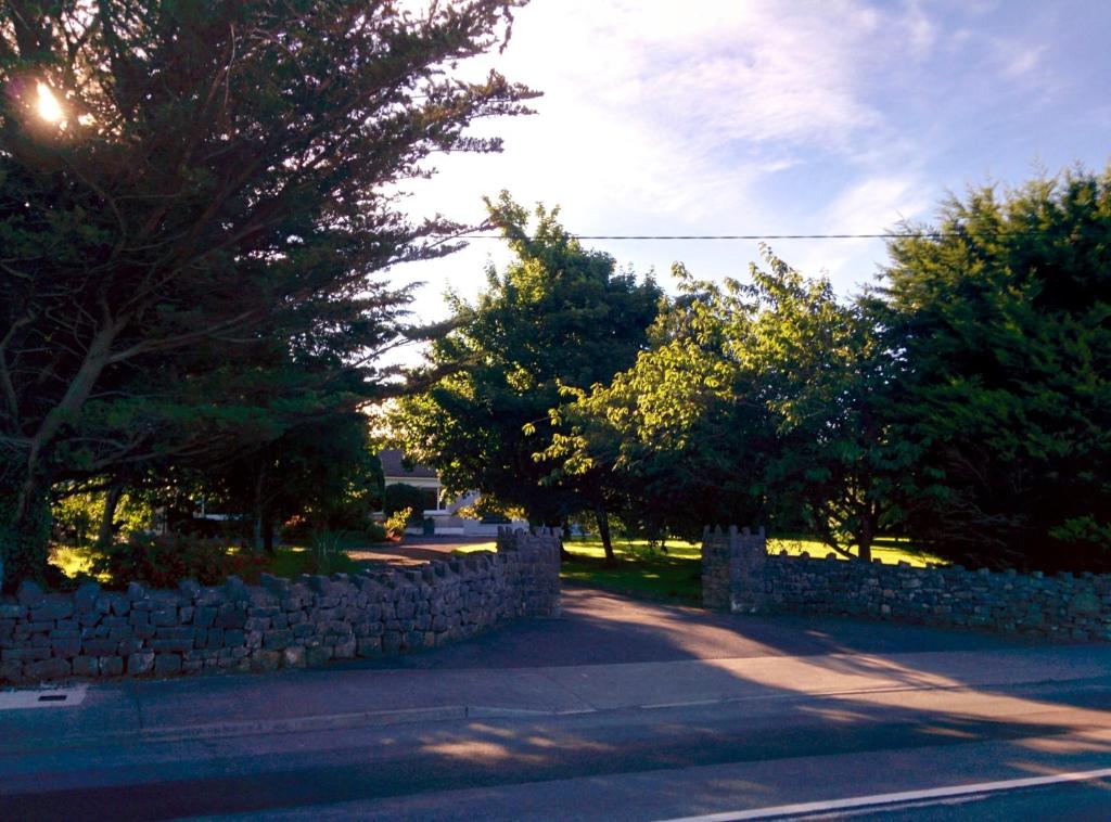 una pared de piedra junto a los árboles y una carretera en Spacious Contemporary Chalet type Apartment., en Galway