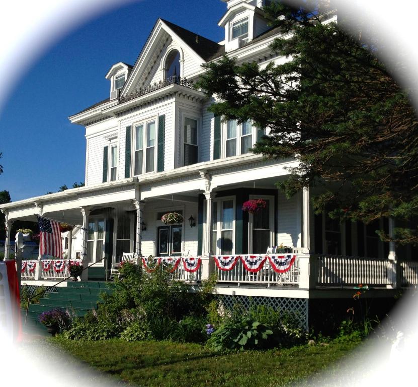una casa blanca con banderas americanas en el porche delantero en Center Harbor Sutton House B & B, en Center Harbor